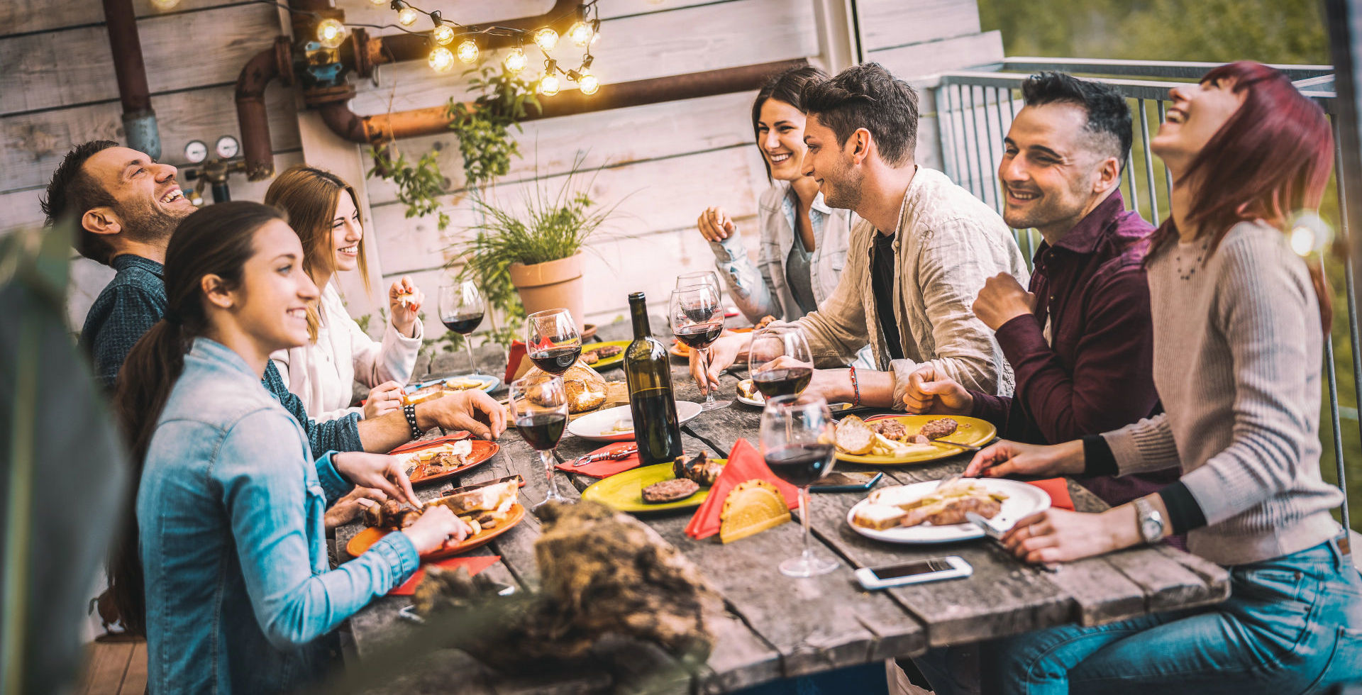 Tisch mit gut gelaunten Menschen, gegrilltem Essen und Wein